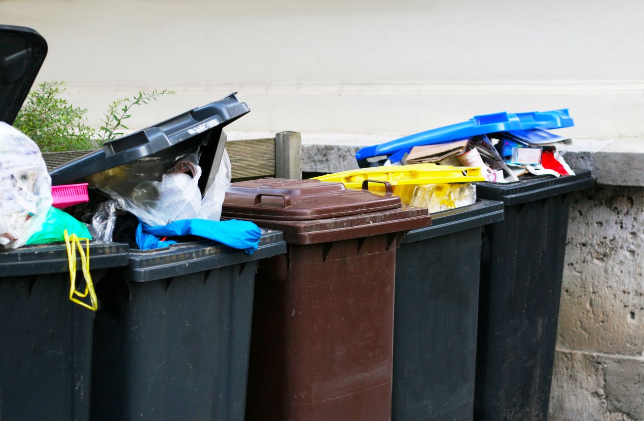 Überfüllte Mülltonnen ohne Mülltonnenbox im öffentlichen Bereich vor einer Hauswand