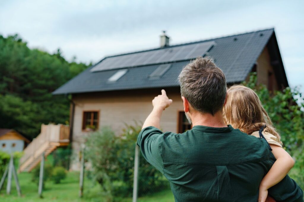Dachbeschichtung im Blick: Hausbesitzer zeigt mit Kind auf das Dach, prüft Zustand der Dachfläche zur Vorsorge