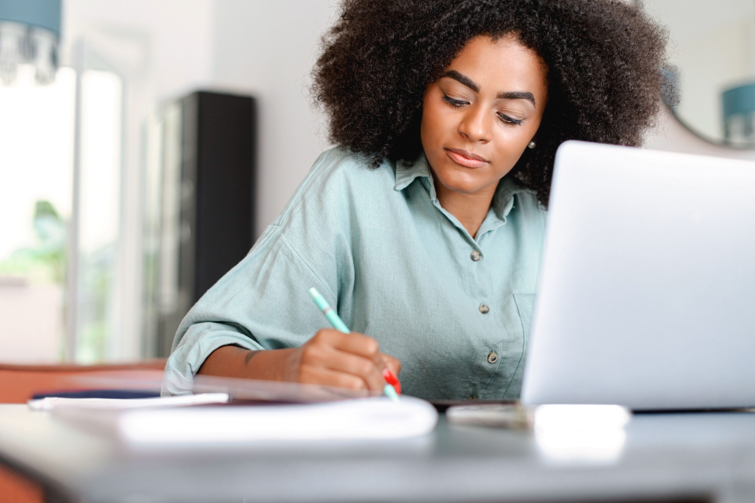 Frau arbeitet konzentriert mit Seminarverwaltungssoftware am Laptop und macht sich handschriftliche Notizen