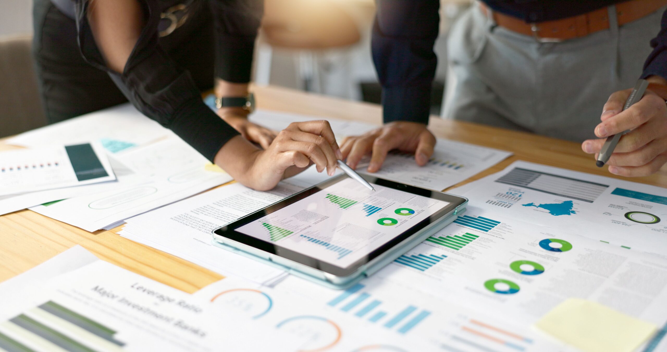 Zwei Personen analysieren mit Seminarverwaltungssoftware Diagramme auf einem Tablet und besprechen Daten zur Planung auf Papier