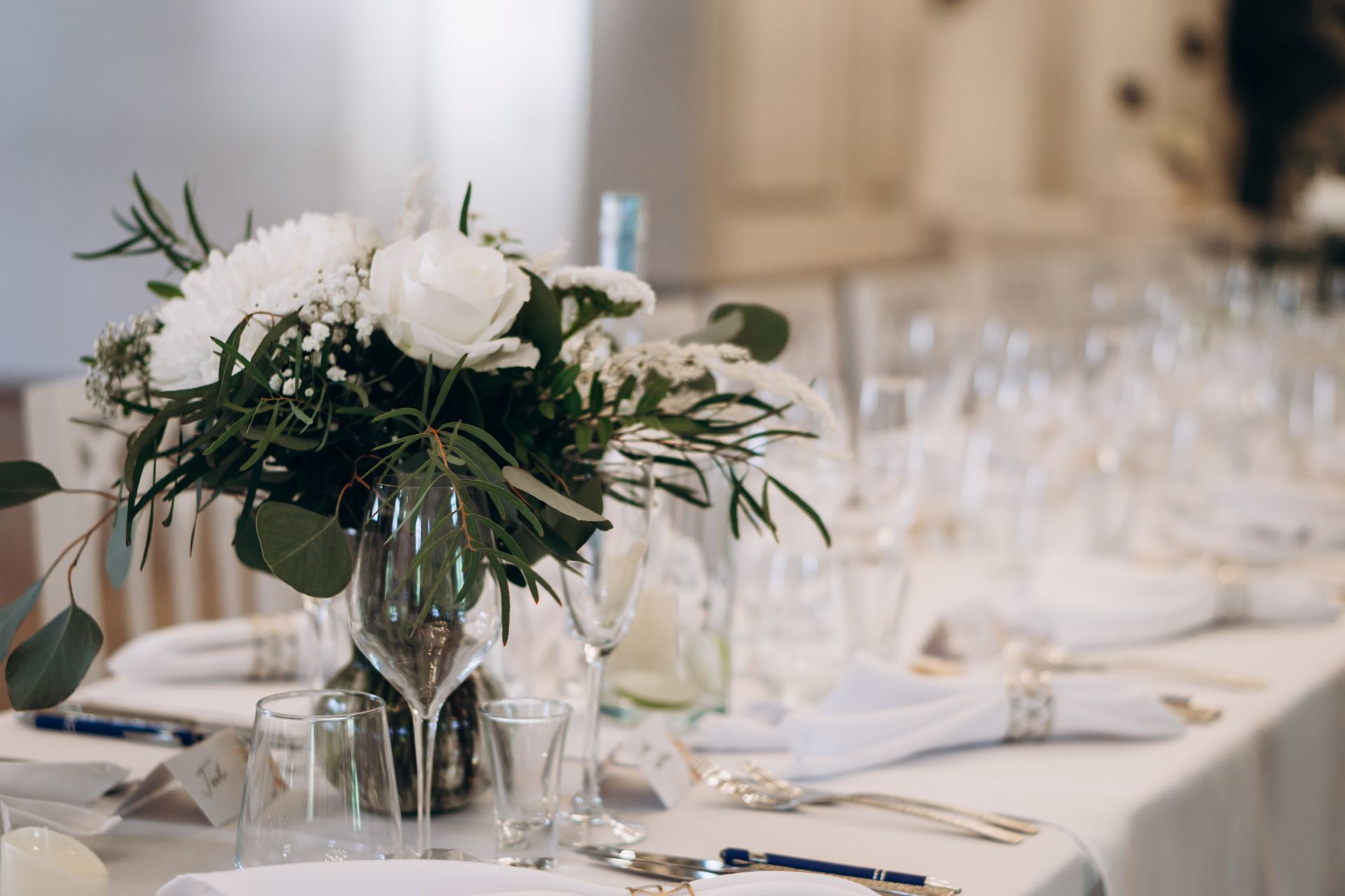 Festlich gedeckter Tisch mit weißen Tischdecken, Gläsern und Blumengesteck für eine elegante Feier