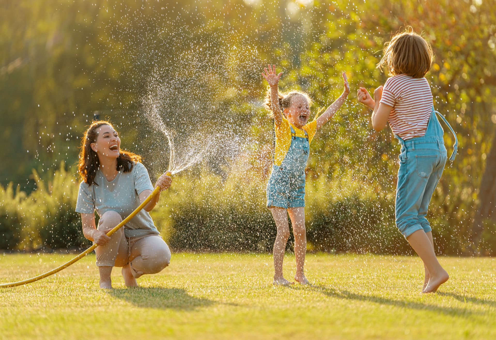 Mutter und Kinder spielen im Garten mit Wasserschlauch – Sommerfreude vor dem eigenen Rundpool