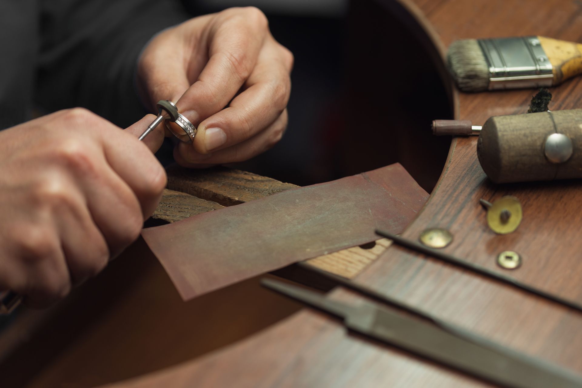 Ein Goldschmied haelt einen Trauring und bearbeitet ihn mit feinem Werkzeug – Darstellung traditioneller Handwerkskunst