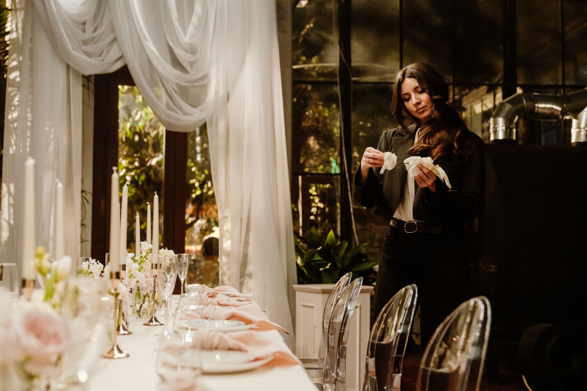 Eventplanerin dekoriert einen langen Tisch mit weißen Tischdecken, Kerzen und Stoffservietten in elegantem Ambiente