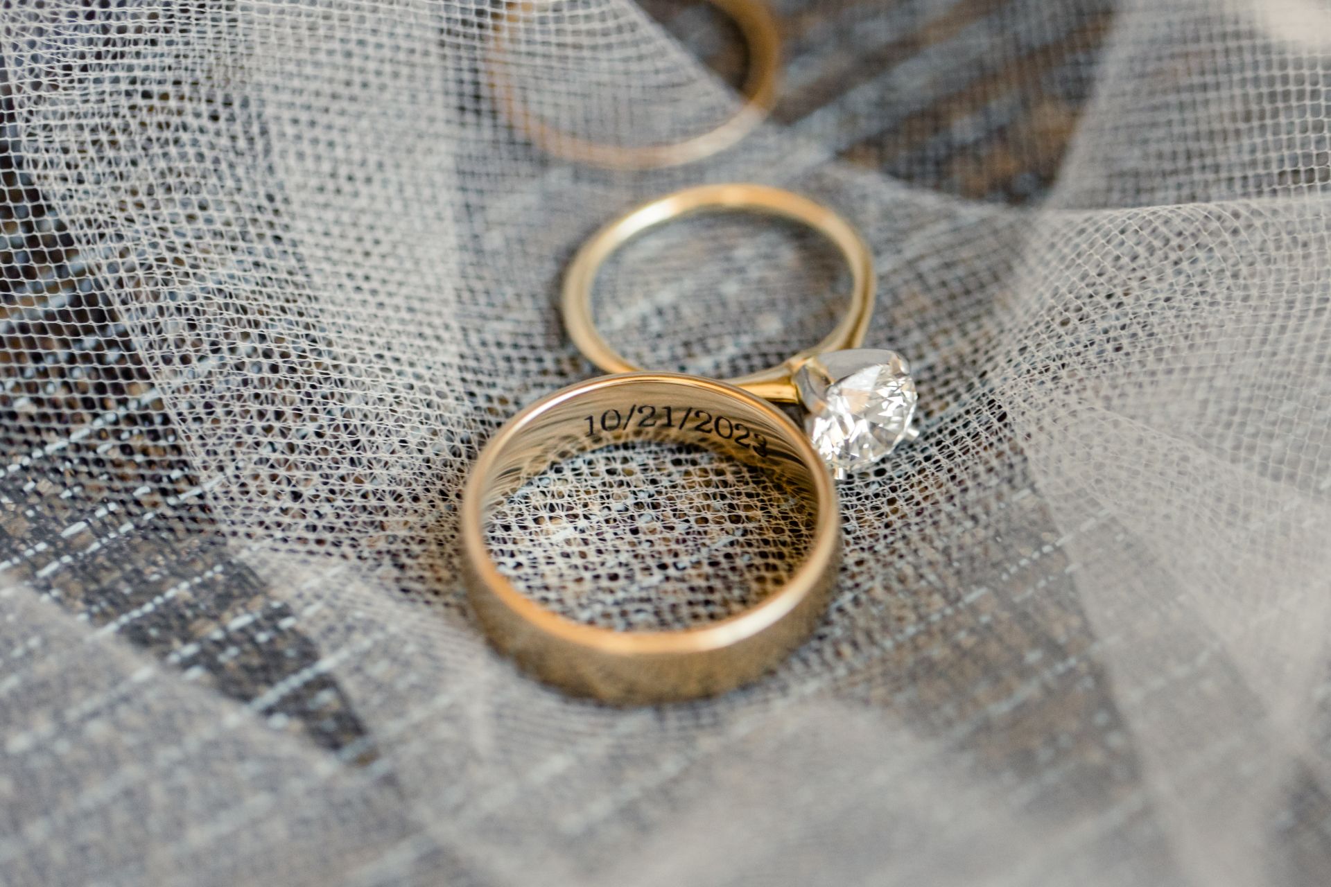 Zwei goldene Trauringe liegen auf feinem Tuell, einer mit Gravur des Hochzeitsdatums – Symbol fuer Individualitaet und Erinnerung