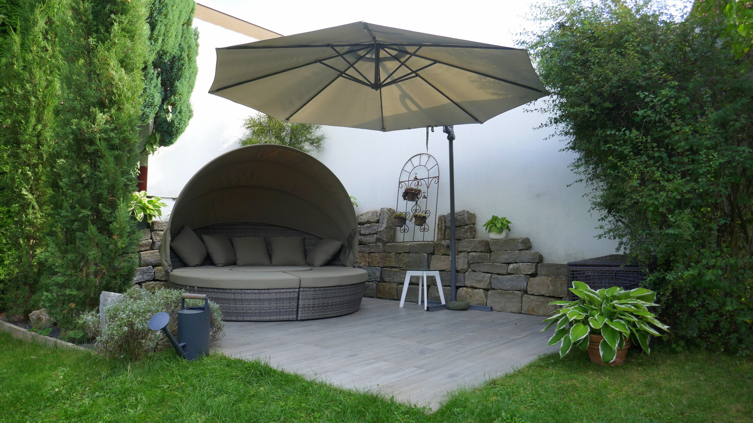 Runde Gartenlounge mit Sonnenschirm und Steinwand | Dekofiguren